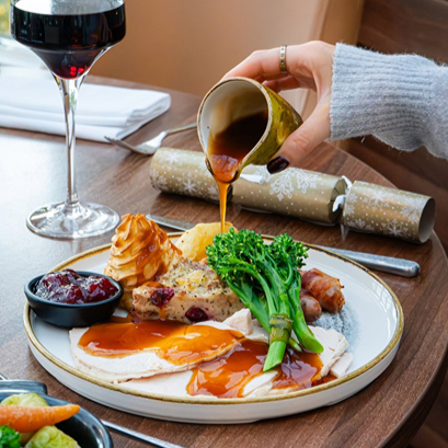 Person pouring gravy over a Christmas dinner