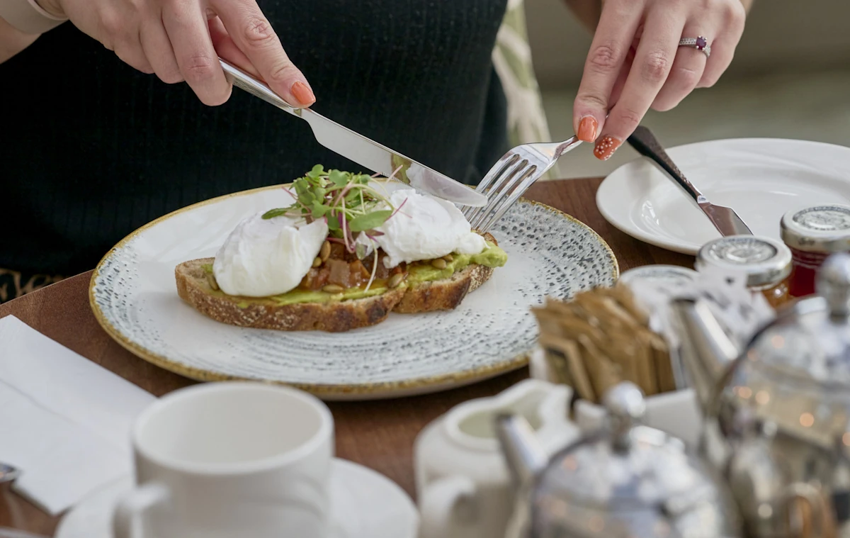 Person cutting up poached egg and avocado on toast