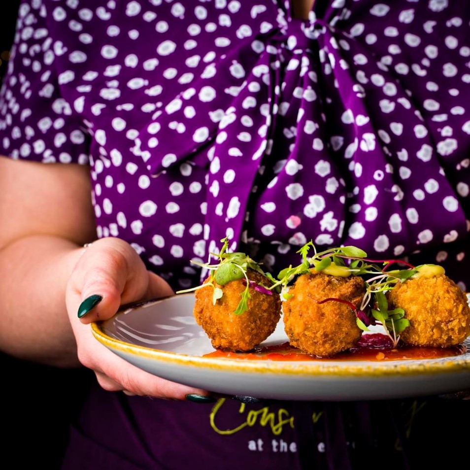 Waiting staff wearing purple The Conservatory uniform and holding a plate of food